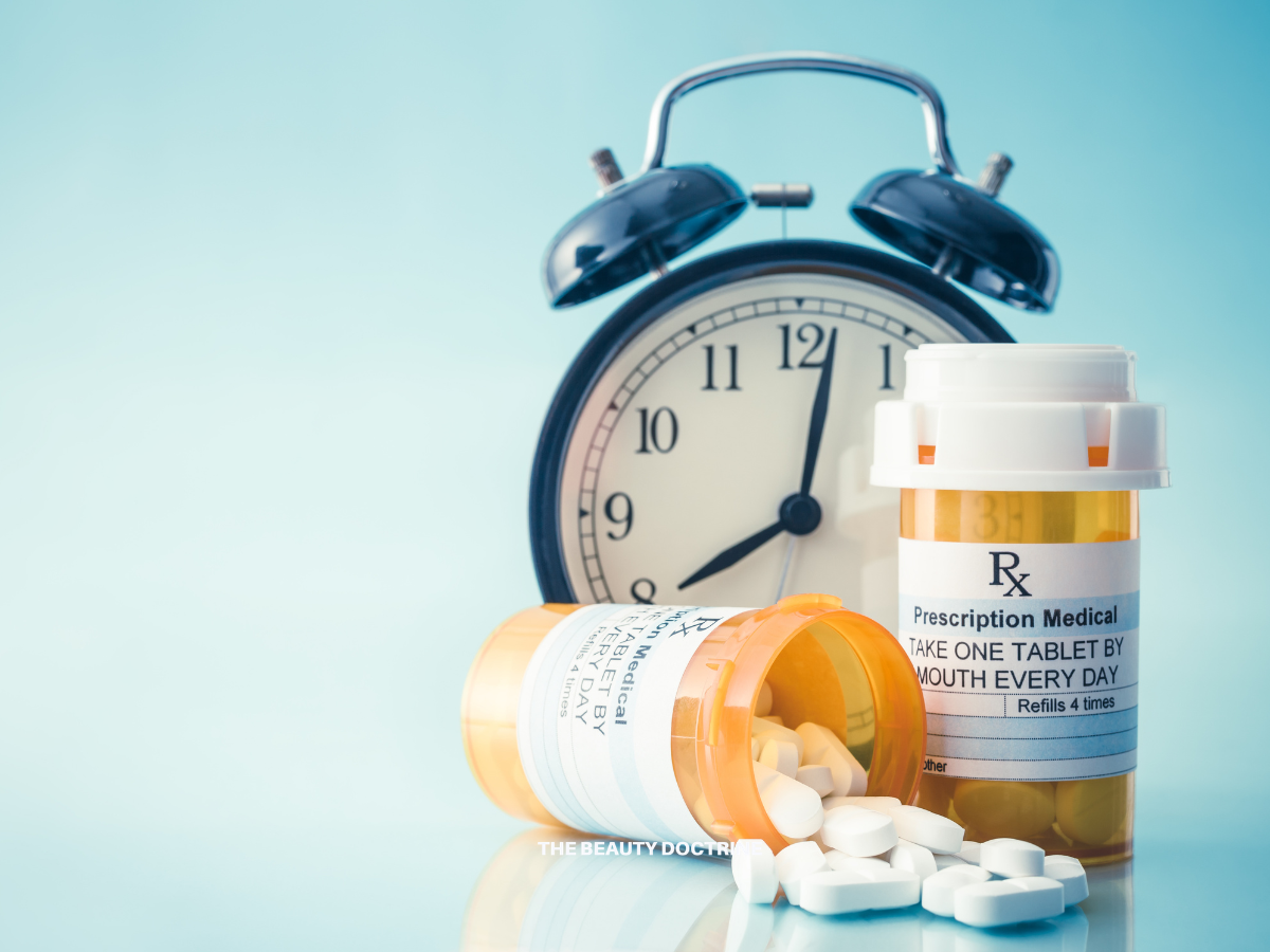 Alarm clock beside two amber prescription bottles and scattered white tablets on a light blue surface.