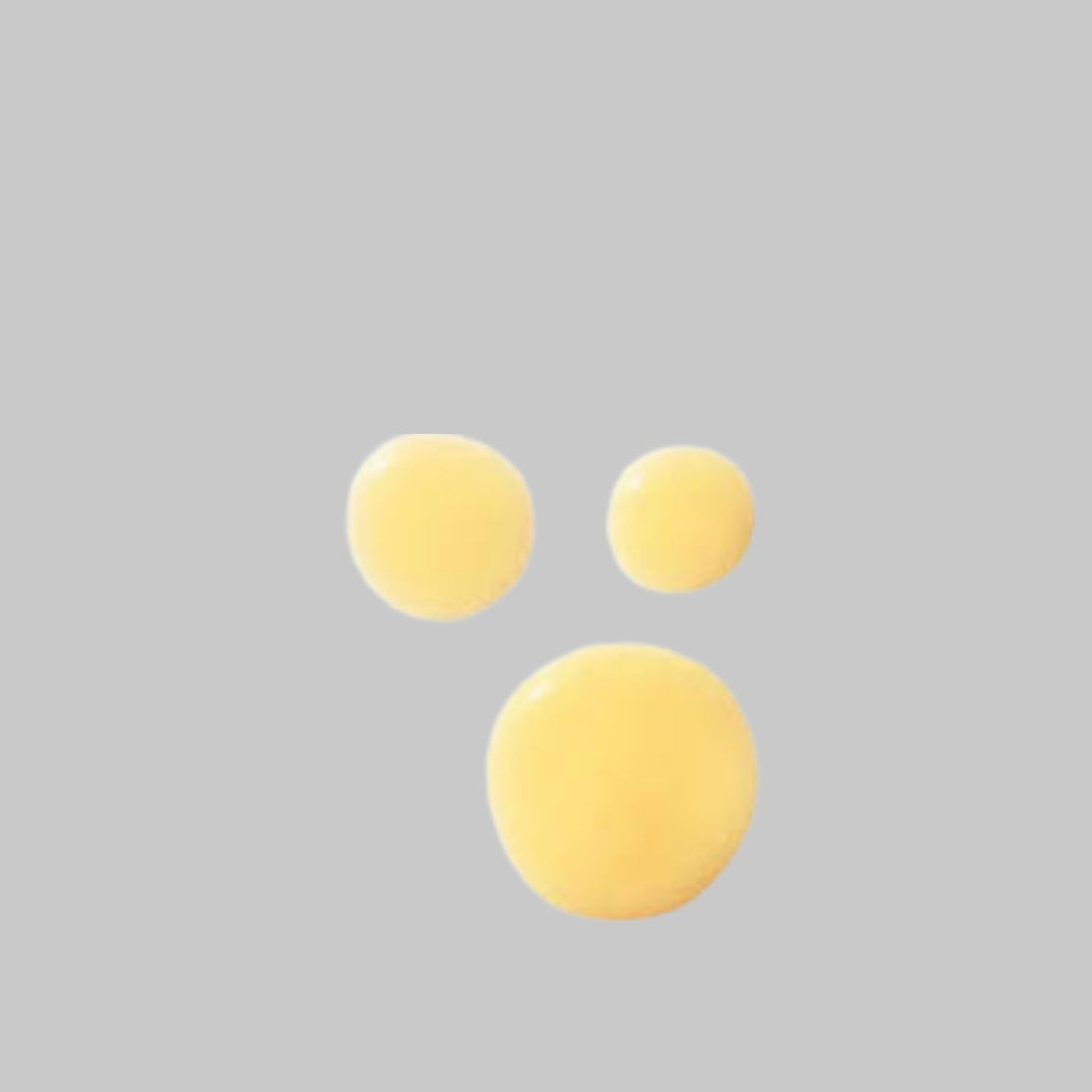 Three golden-yellow drops of Agent Nateur Body (Balm) showing the crème’s texture.