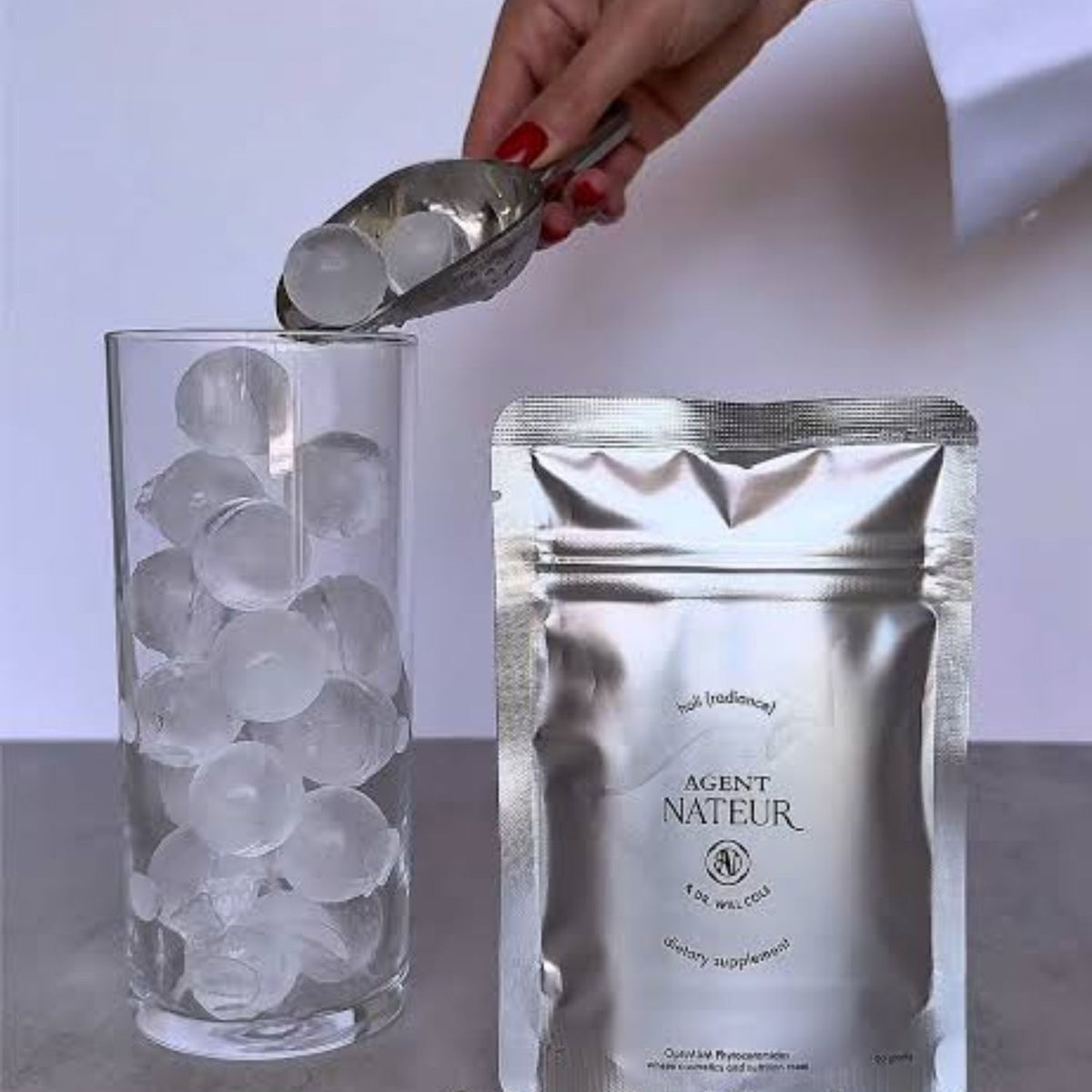 Agent Nateur holi (radiance) silver pouch beside a tall glass as ice is added.