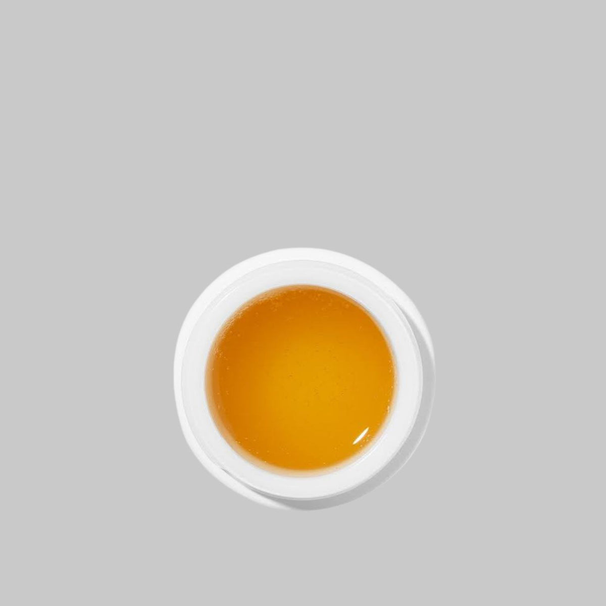 Top view of an open Agent Nateur holi (bright) face mask jar showing its glossy amber gel texture