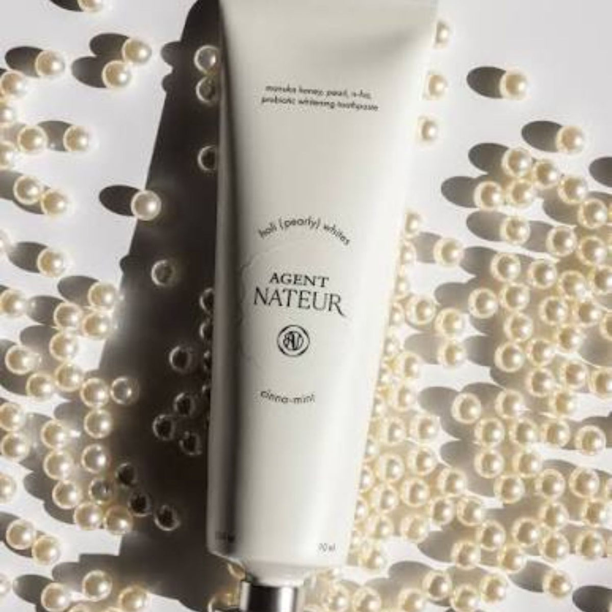 Agent Nateur holi (pearly) whites probiotic whitening toothpaste tube surrounded by pearls on a white background
