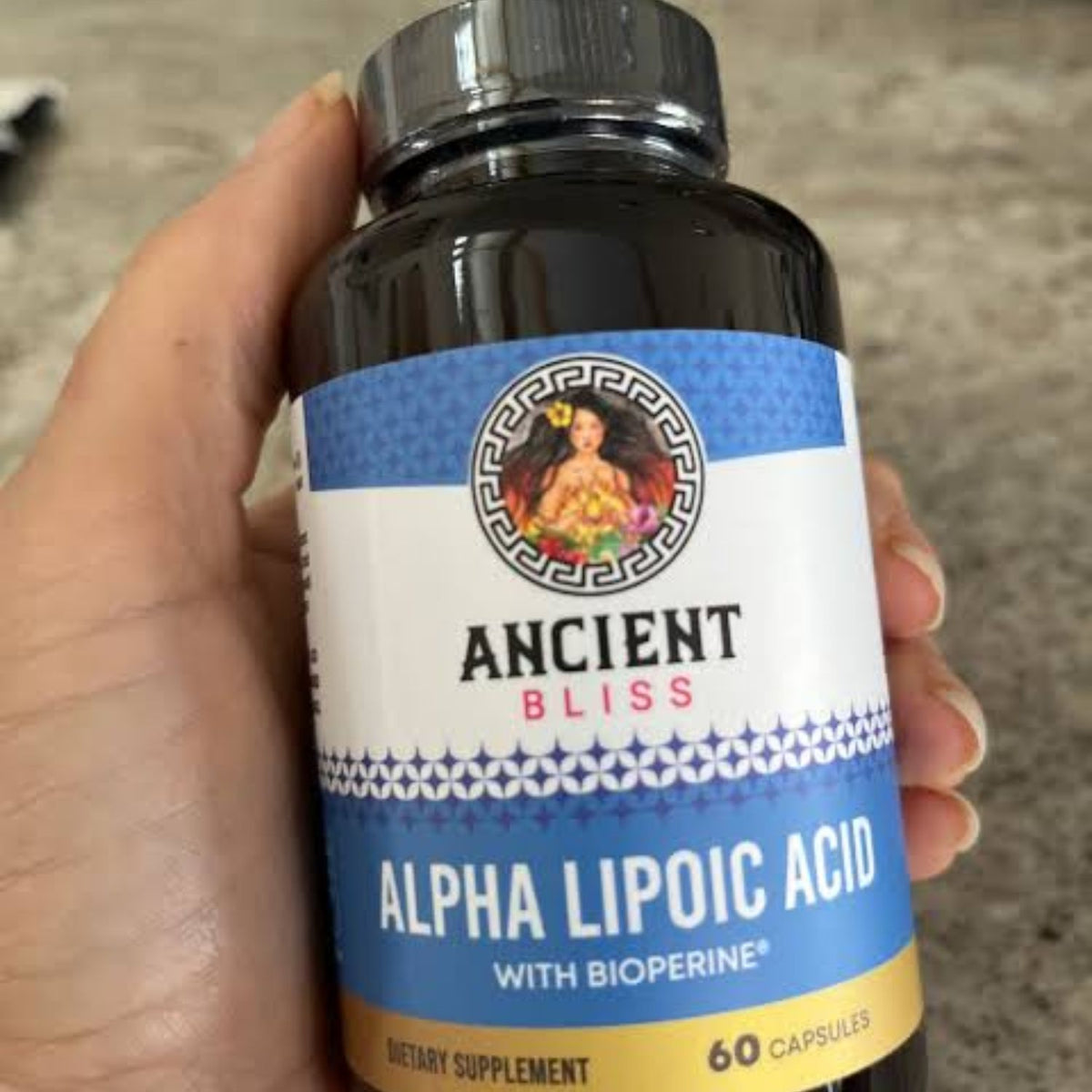 Hand holding an Ancient Bliss Alpha Lipoic Acid with BioPerine bottle, 60 capsules.