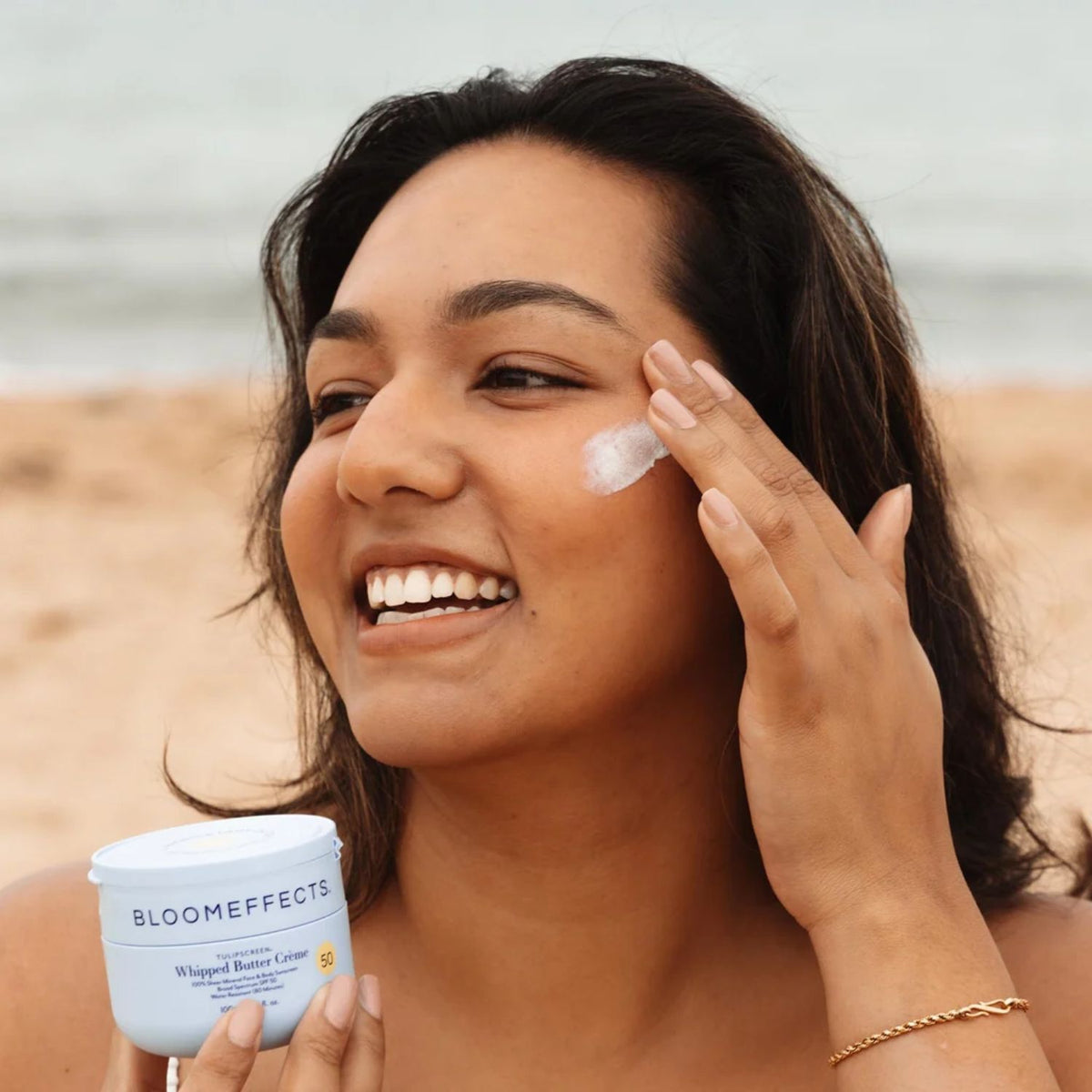 Woman applying Bloomeffects Tulipscreen Whipped Butter Crème SPF 50 to her cheek while holding the open jar.