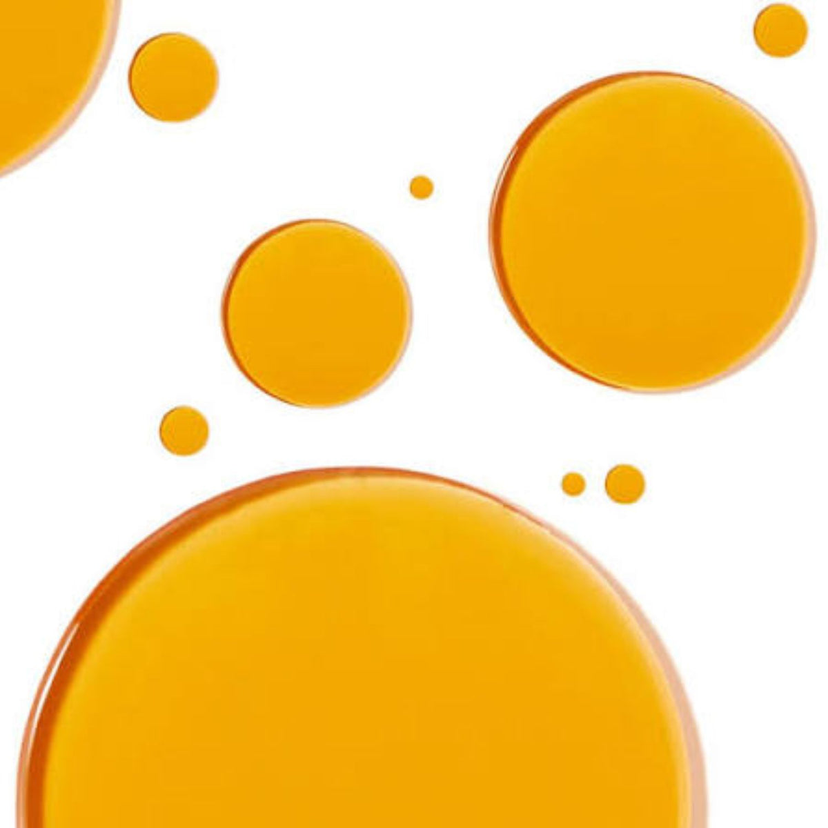 Golden drops of Kari Gran Vitamin C Serum showing its oil texture on a white background.