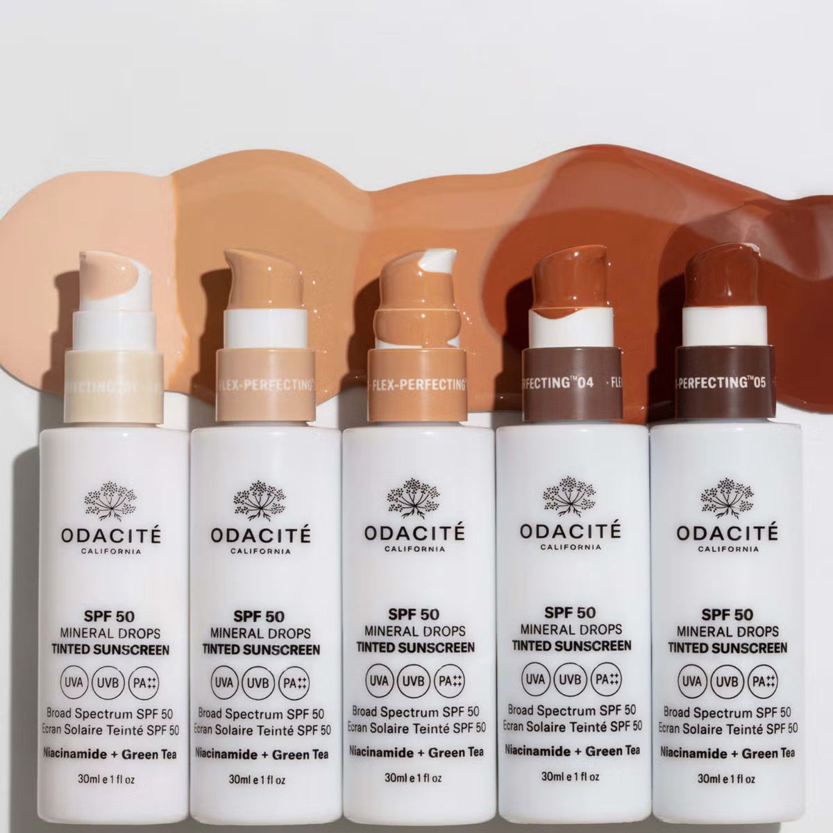 Five Odacité SPF 50 tinted mineral sunscreen bottles lined up beneath matching swatches from light beige to deep brown.