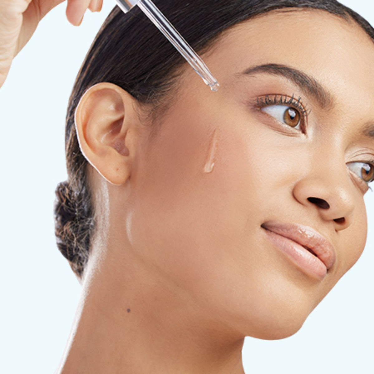 Application image: Woman applying a drop of serum to her cheek with a glass dropper.