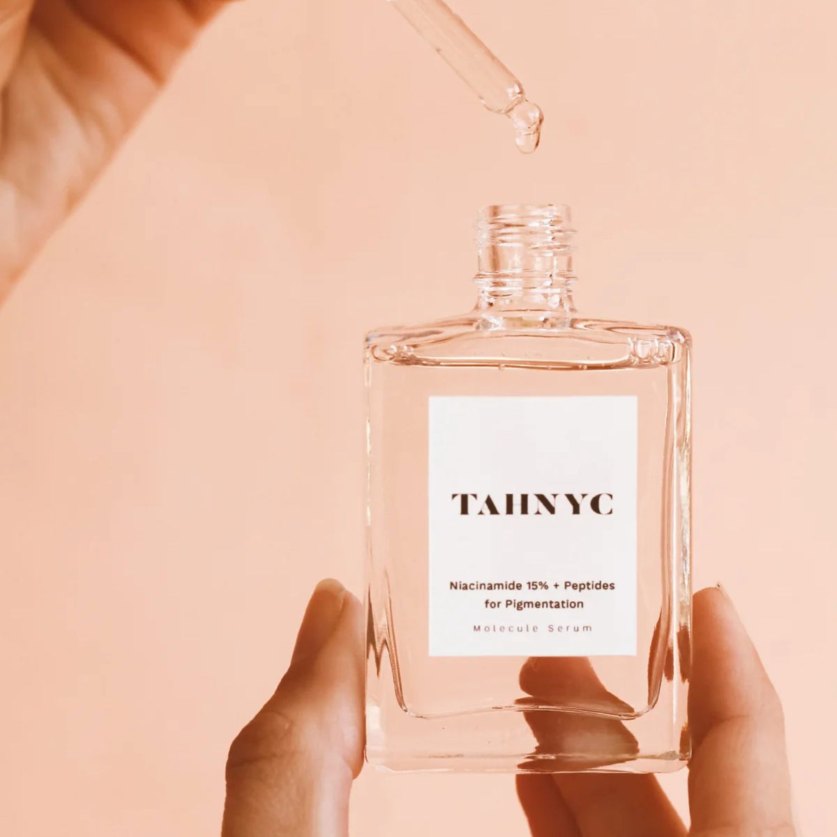 Hand holding TAHNYC Niacinamide 15% + Peptides for Pigmentation serum with a dropper above the open bottle.