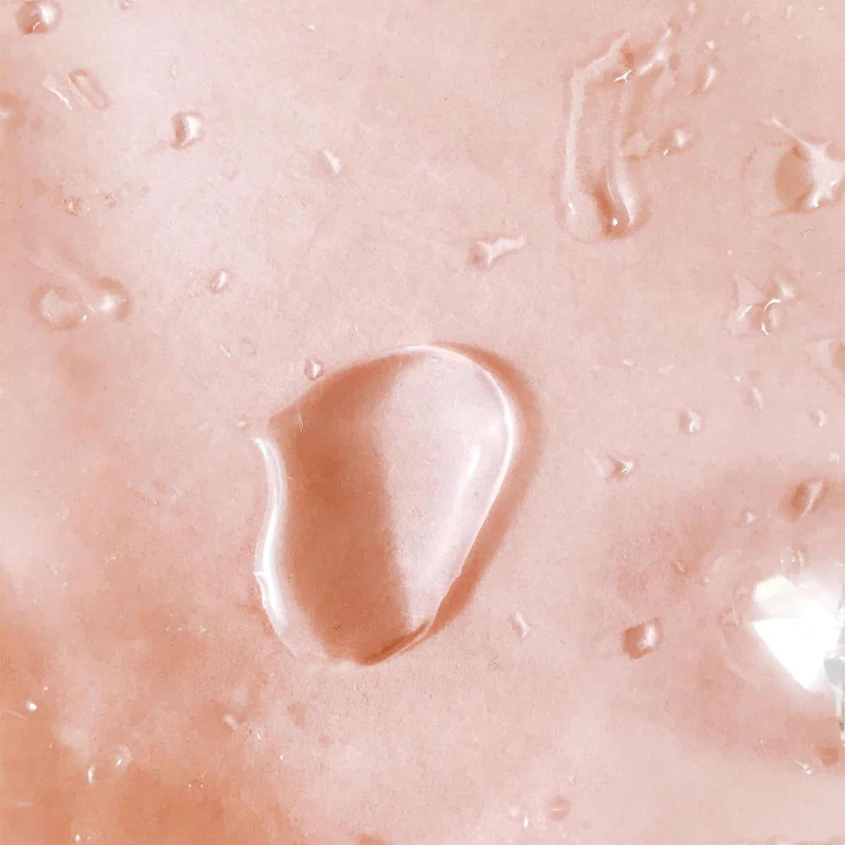 Close-up of clear TAHNYC Niacinamide 15% + Peptides face serum droplets on a peach background