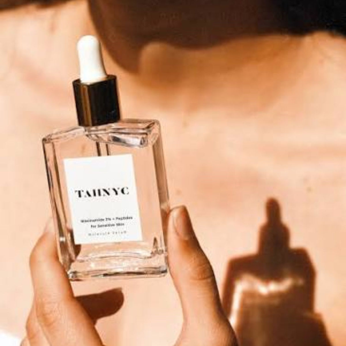 Hand holding TAHNYC Niacinamide 3% + Peptides serum bottle in warm sunlight