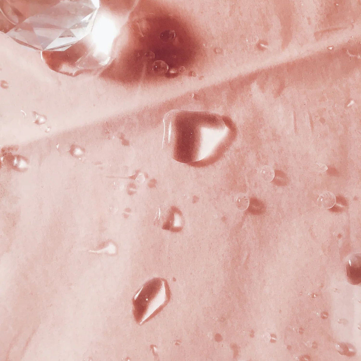 Clear serum droplets on a pink background, showing the texture of TAHNYC Niacinamide 3% + Peptides.