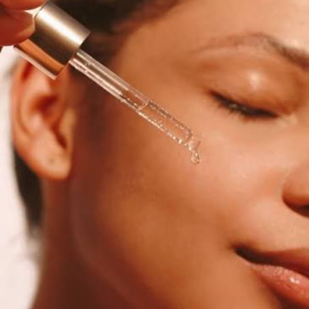 serum application: “Close-up of a dropper dispensing TAHNYC Niacinamide 5% + Peptides serum onto a woman’s cheek.