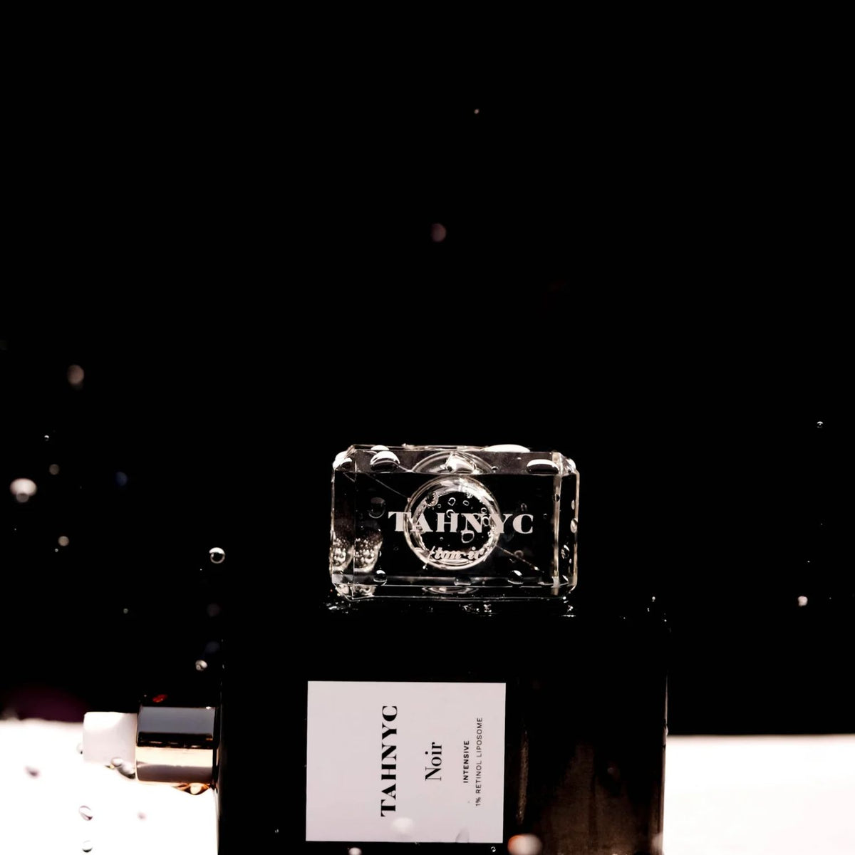 TAHNYC Noir Intensive Retinol Liposome bottle with water droplets against a black background.

