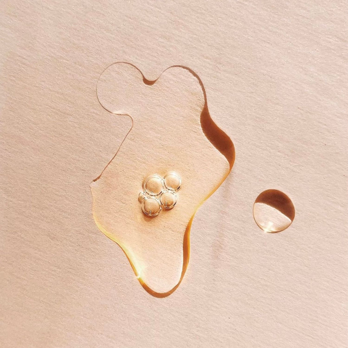 Golden TAHNYC Noir retinol serum with air bubbles on a peach background.

