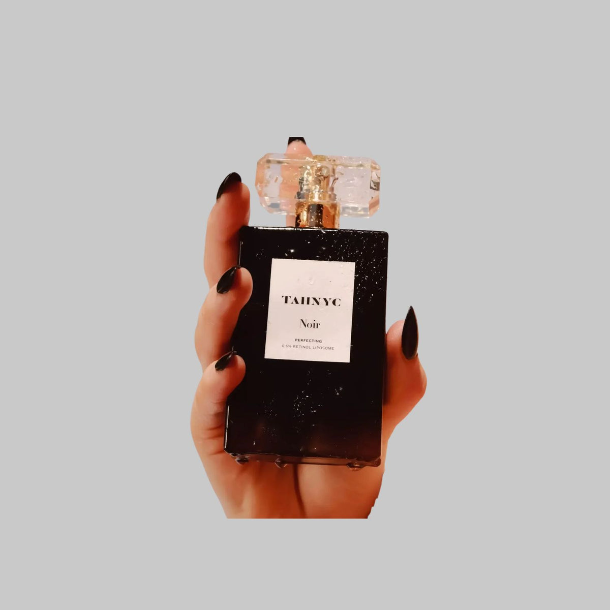Hand holding a black bottle of TAHNYC Noir Perfecting 0.5% Retinol Liposome Face Serum with a clear cap