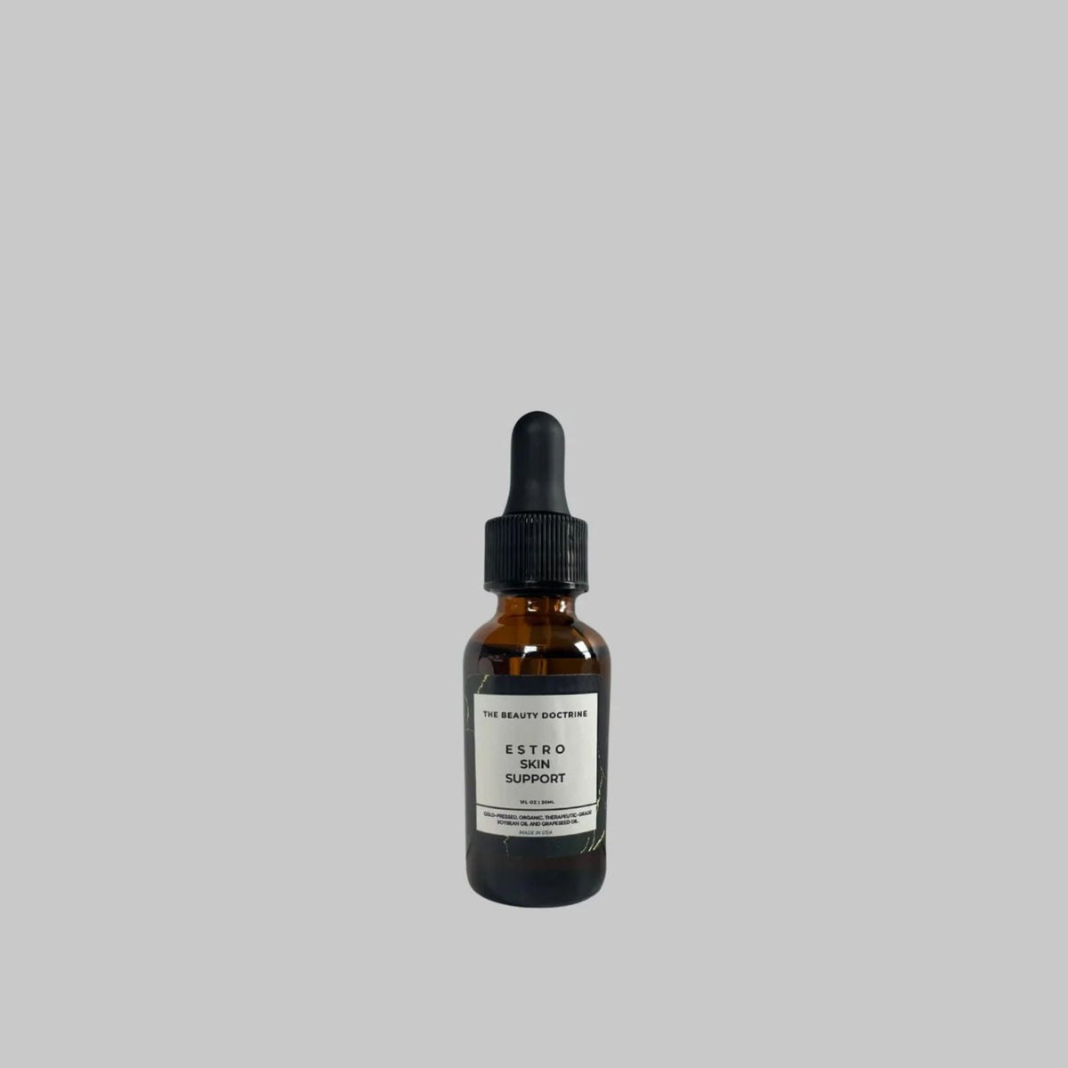 The Beauty Doctrine Estro Skin Support Serum in an amber glass bottle with a black dropper on a gray background.
