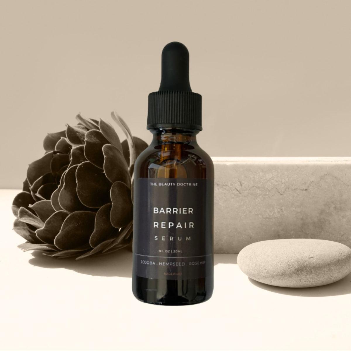 The Beauty Doctrine Barrier Repair Serum in an amber dropper bottle beside a dried flower and smooth stone.