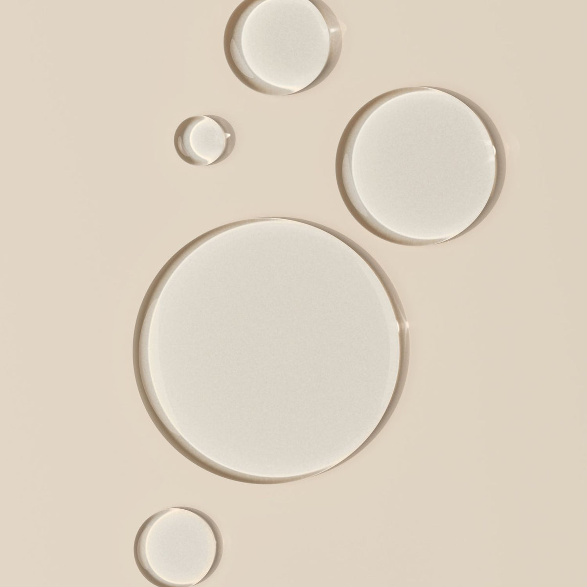 Five clear oil droplets of varying sizes on a beige background.