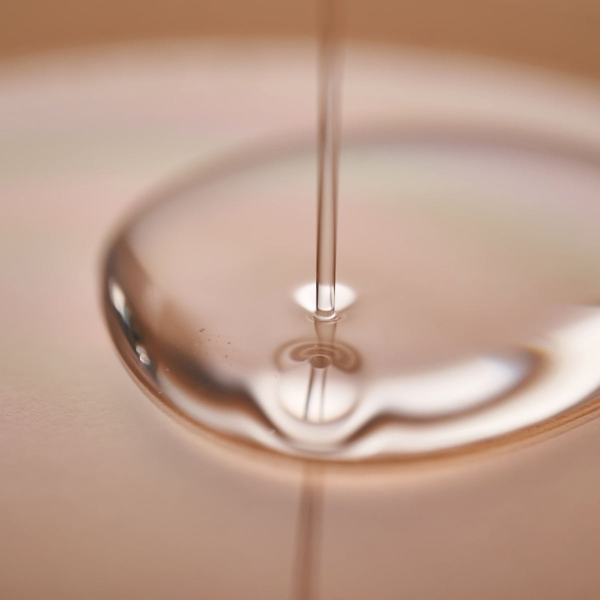 Close up of hair serum oil flowing into a glossy pool