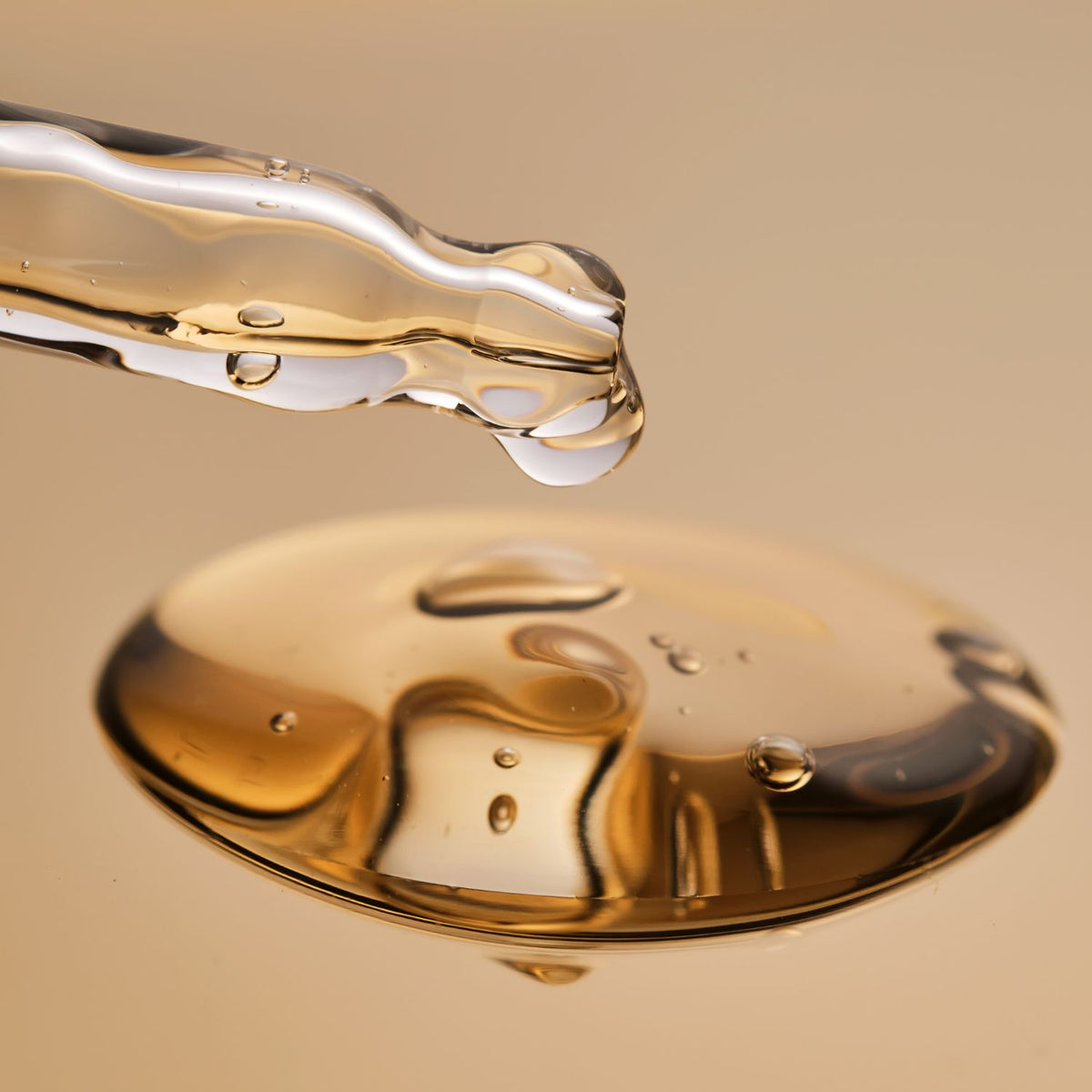 oil texture: Close-up of golden plum oil dripping from a glass dropper above a pool of oil.