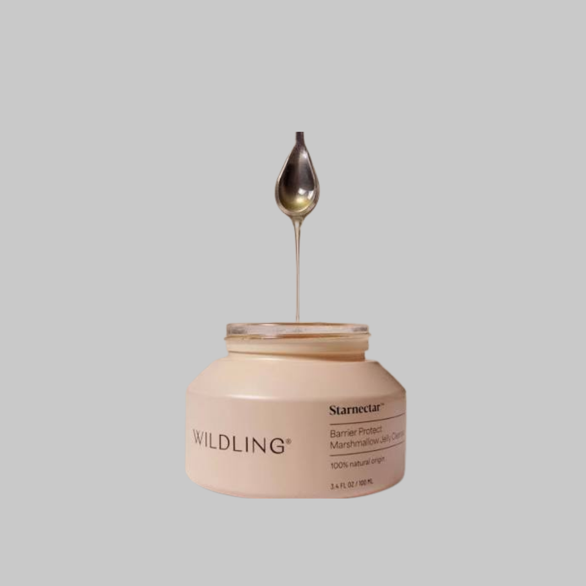 Golden jelly cleanser dripping from a spoon into an open jar of Wildling Starnectar Jelly Cleanser.